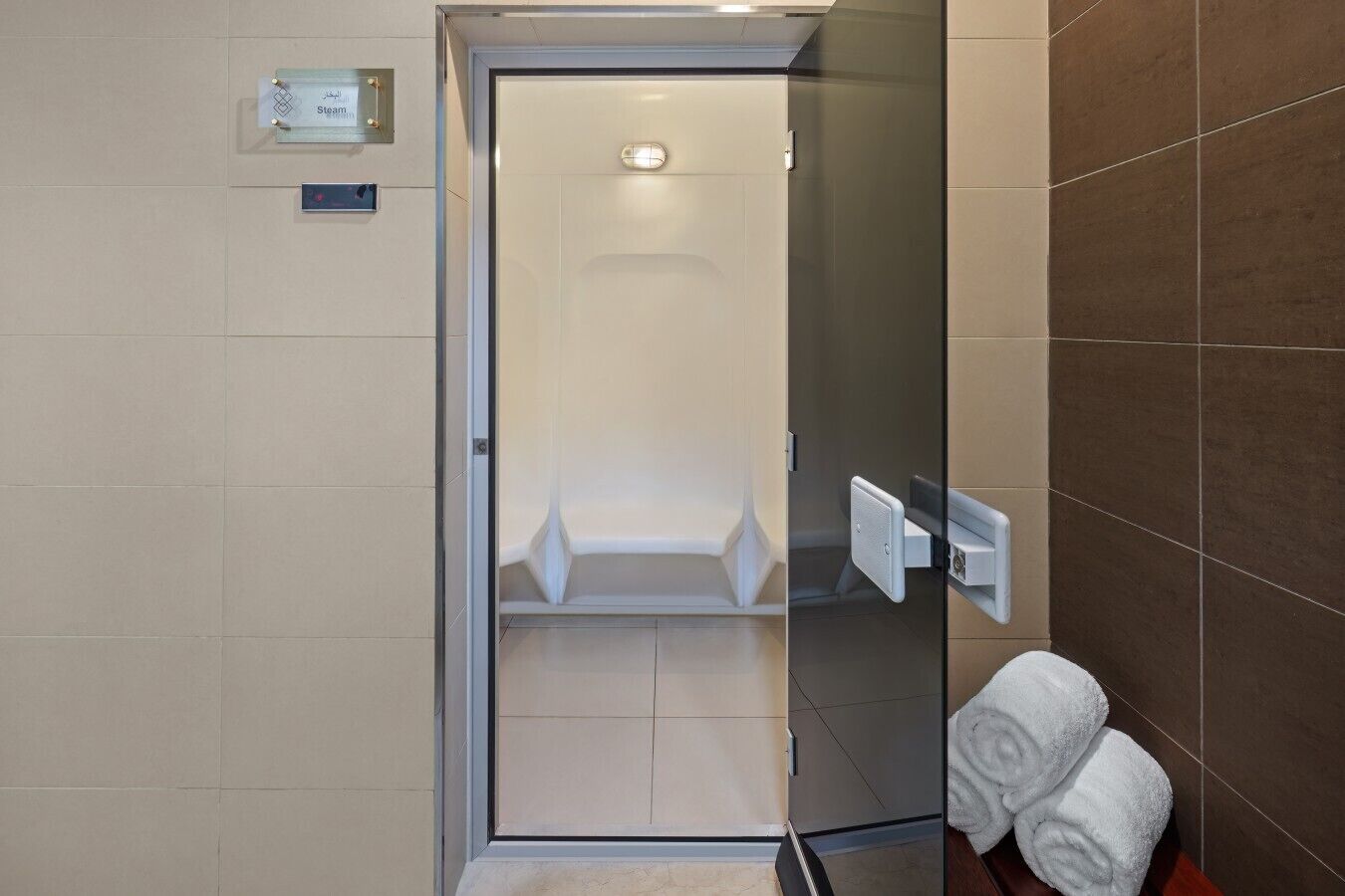 Une salle de bain moderne dotée d’une douche à parois de verre, d’un porte-serviettes avec des serviettes et d’un panneau de commande visible.