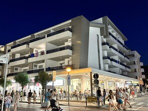 Ein mehrstöckiges Gebäude mit Balkonen, ein Restaurant im Erdgeschoss und ein Fußgängerbereich mit Personen.