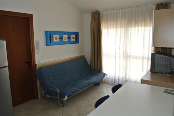 Quarto com um sofá azul, uma mesa branca, uma televisão e uma porta.