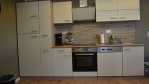 A compact kitchen with white cabinets, a built-in oven, and a coffee maker on the countertop. - Ferienwohnung Klüger - Vacation for the small family (Liebstadt)