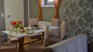 A dining area with a table set for four, chairs, a window with curtains, and a patterned wallpaper. - Ferienwohnung Klüger - Vacation for the small family (Liebstadt)