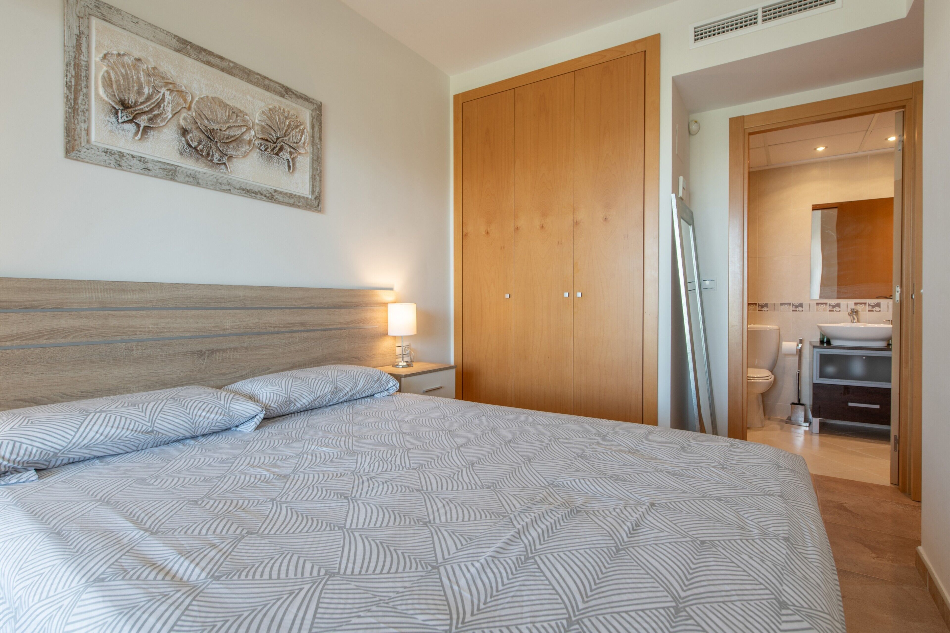 Un dormitorio con cama, armario de madera, baño con lavamanos y un cuadro en la pared.