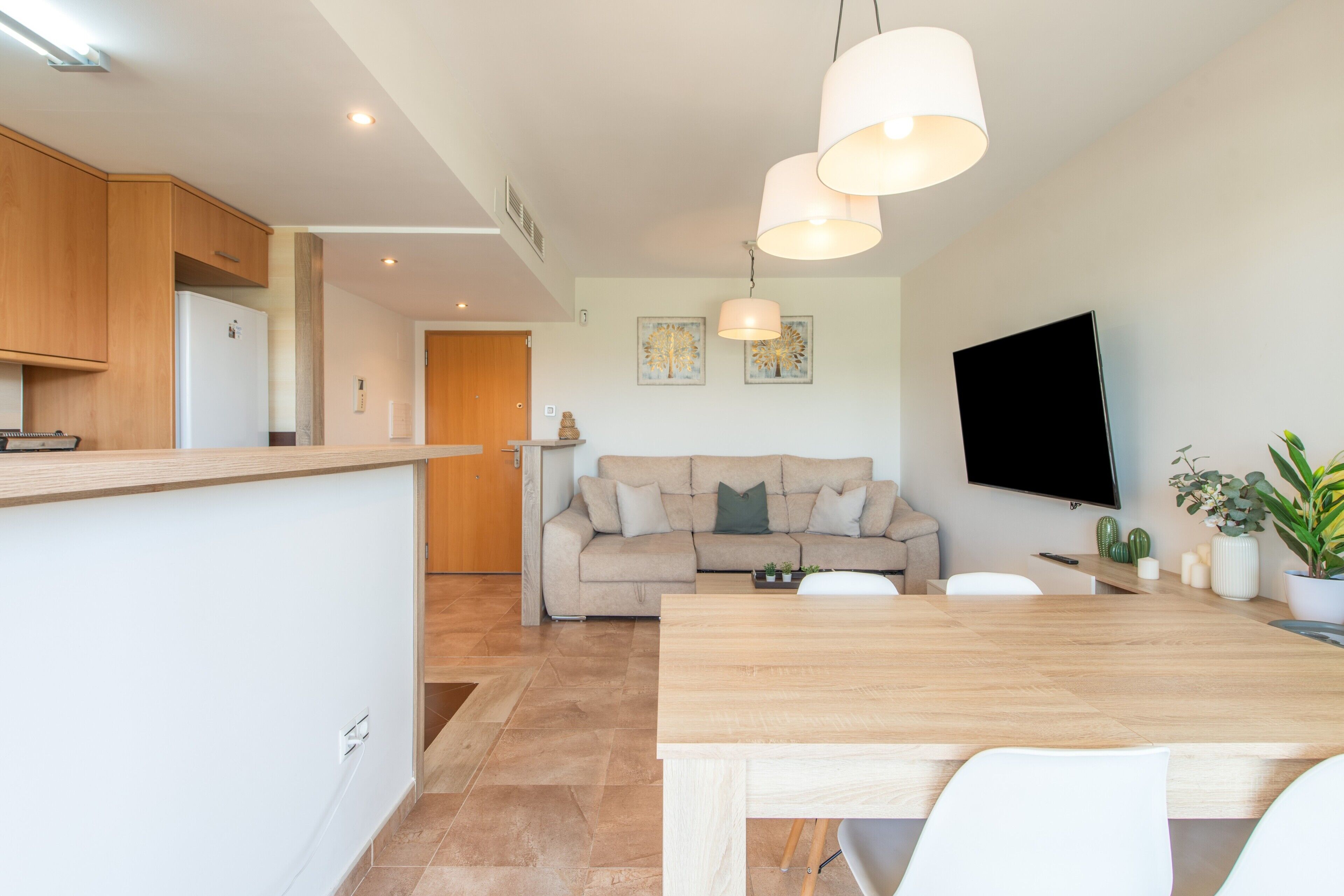 Une cuisine moderne avec des meubles en bois, un coin repas comprenant une table et des chaises en bois, un canapé et un téléviseur à écran plat fixé au mur.