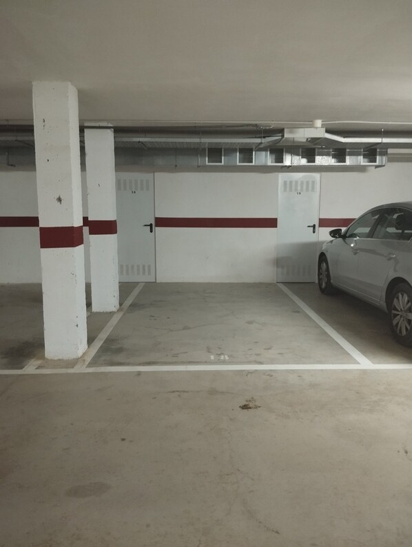 A parking garage with white pillars, red stripes, and a white car parked in one of the spaces.