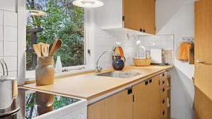 Eine moderne Küche mit einem großen Fenster, Holzschränken, einer Edelstahlspüle und einem Wasserkocher auf der Arbeitsplatte.