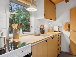 Una cocina moderna con un ventanal grande, armarios de madera, un lavamanos de acero inoxidable y una tetera sobre la encimera.