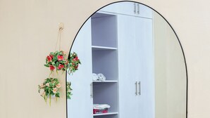 A room with a white wardrobe, a mirror, a white furry rug, and a hanging plant. - 2-bedroom apartment in peaceful Kampala with AC for relaxing stays (Kampala)