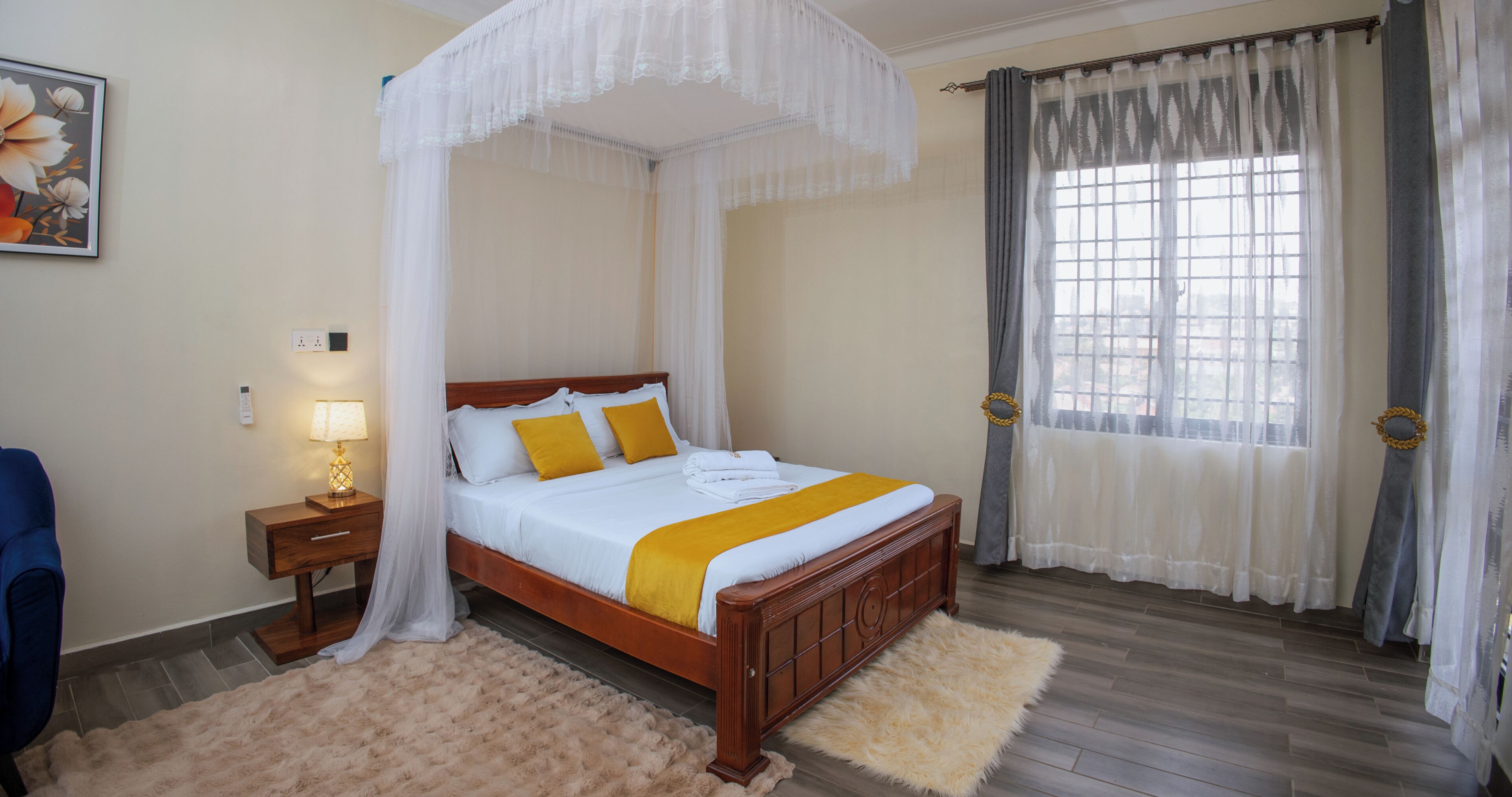 Quarto com cama de dossel, mesa de cabeceira com abajur, tapete felpudo e janela com cortinas.
