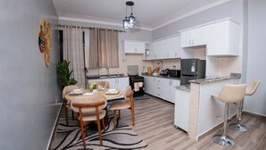 A compact kitchen with a dining area, a bar stool, and a refrigerator. - 2-bedroom apartment in peaceful Kampala with AC for relaxing stays (Kampala)