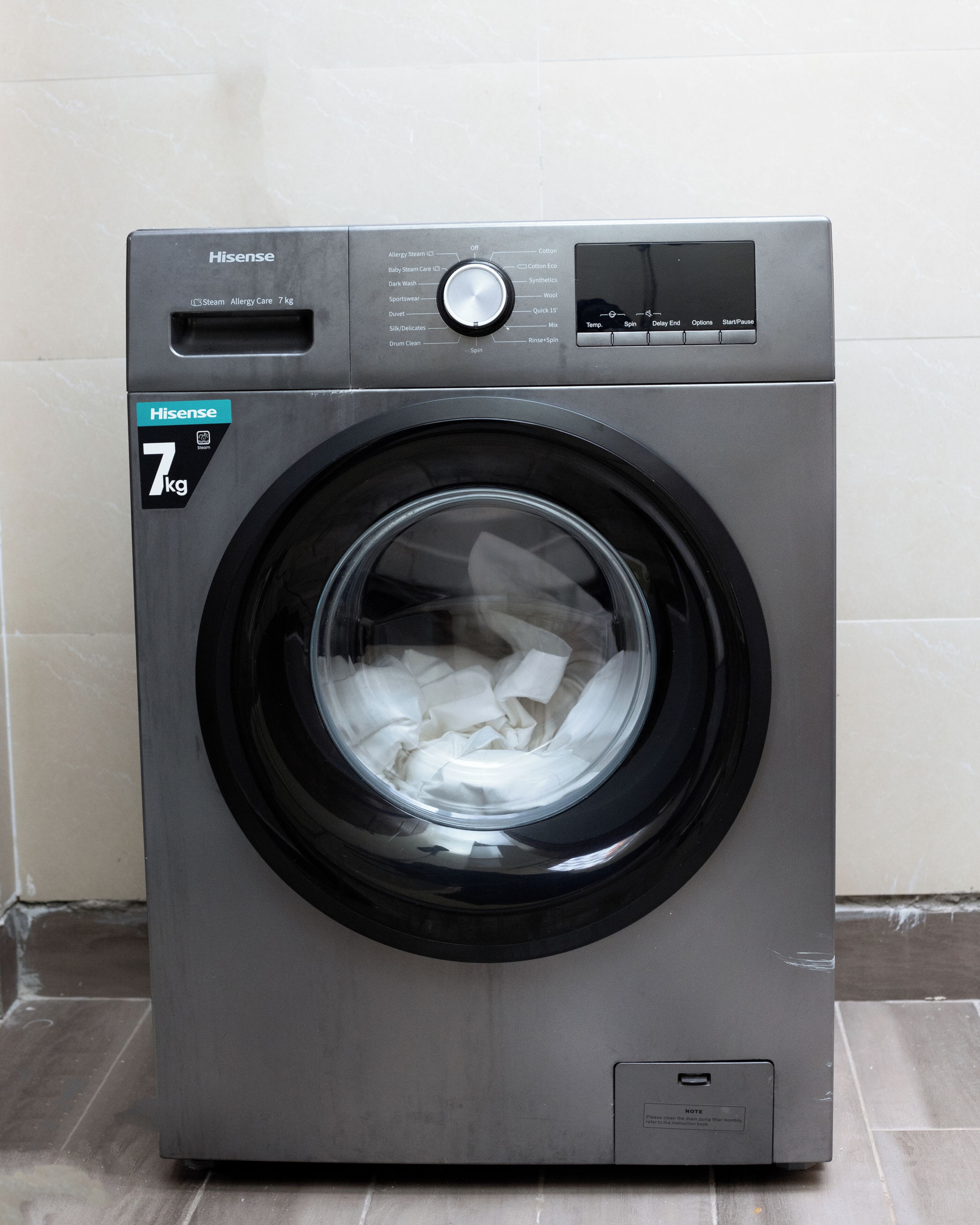 Une machine à laver Hisense de 7 kg à chargement frontal, dotée d’une porte transparente, d’un panneau de commande et d’une indication précisant qu’il ne faut pas ouvrir la porte pendant le fonctionnement de l’appareil.