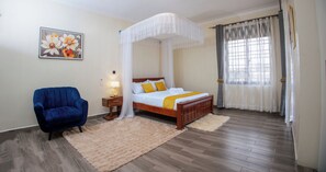 A bedroom with a four-poster bed, a blue armchair, a fluffy rug, and a painting on the wall. - 2-bedroom apartment in peaceful Kampala with AC for relaxing stays (Kampala)