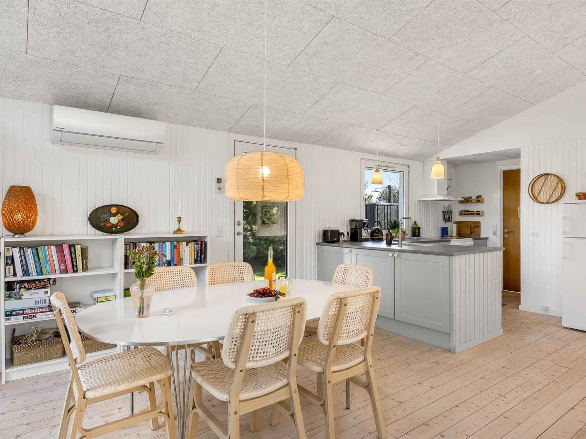 A modern kitchen with white cabinetry, a central island, and a dining area with wicker chairs and a white table.