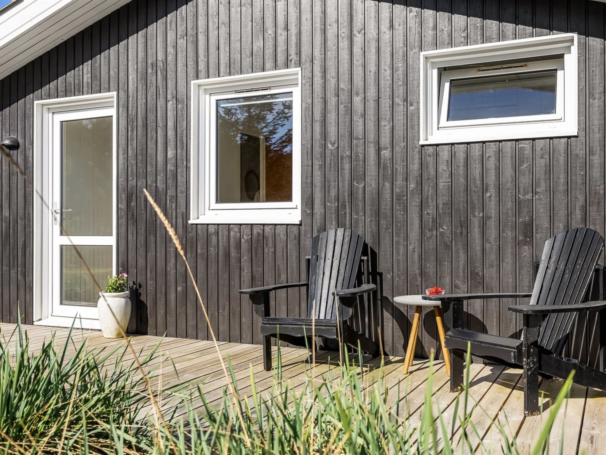 Een houten gevel met twee ramen, een deur en terrasmeubels met stoelen en een tafel.