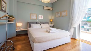 A bedroom with a bed, bedside lamps, a hanging light fixture, a wall-mounted air conditioner, and a window with curtains. - Cozy Apartment with Beautiful Balcony (Athina)