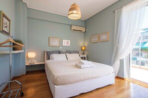 A bedroom with a bed, bedside lamps, a hanging light fixture, a wall-mounted air conditioner, and a window with curtains. - Cozy Apartment with Beautiful Balcony (Athina)