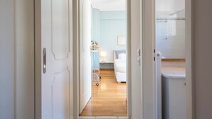 A hallway leading to a bedroom with a bed, bedside table, and a small cart. - Cozy Apartment with Beautiful Balcony (Athina)