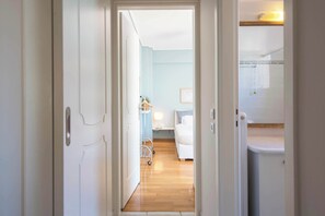 A hallway leading to a bedroom with a bed, bedside table, and a small cart. - Cozy Apartment with Beautiful Balcony (Athina)