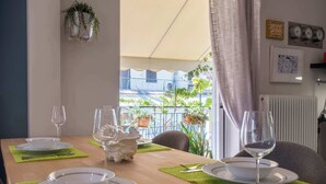 A dining table set with plates, cutlery, and wine glasses, with a view of a balcony and outdoor plants. - Cozy Apartment with Beautiful Balcony (Athina)
