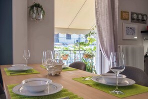 A dining table set with plates, cutlery, and wine glasses, with a view of a balcony and outdoor plants. - Cozy Apartment with Beautiful Balcony (Athina)