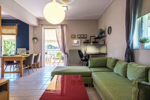 A living room with a green sofa, a wooden dining table with chairs, a red coffee table, and a large window with curtains. - Cozy Apartment with Beautiful Balcony (Athina)