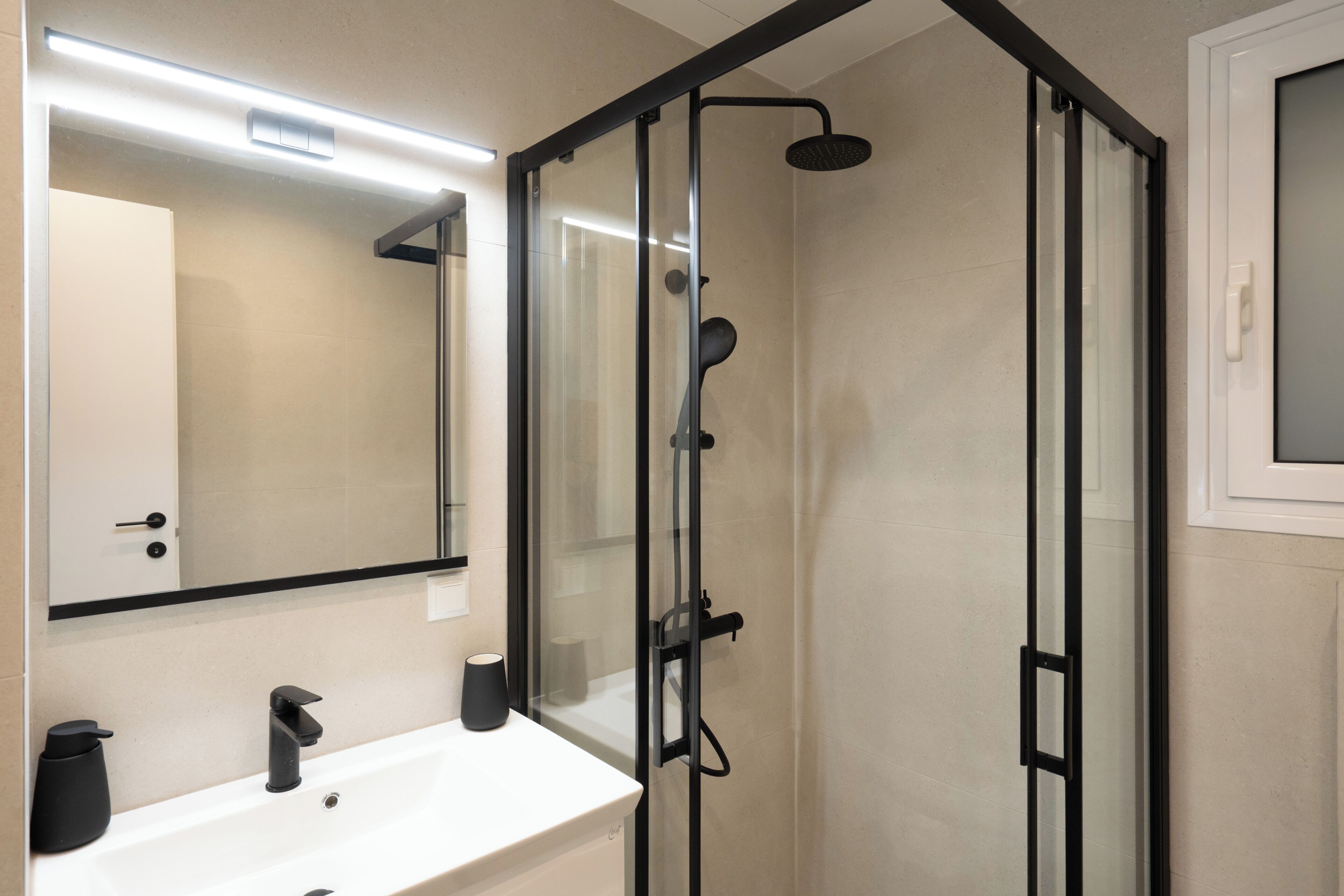 A modern bathroom with a glass-enclosed shower, a white sink, and a mirror above the sink.