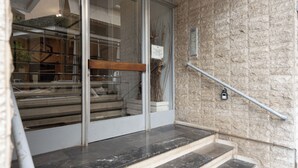 Una escalera con barandilla de metal, pared de piedra y puerta de cristal que da a un espacio interior.