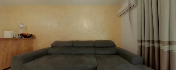 A living room with a dark grey sofa, a wooden cabinet, an air conditioning unit, and a curtain. - Charming 3-bedroom House Rental in Málaga, Spain (Málaga)