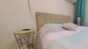 A bed with a tufted headboard, a bedside table with a wireless charger, and a window with curtains. - Charming 3-bedroom House Rental in Málaga, Spain (Málaga)