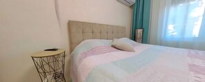A bed with a tufted headboard, a bedside table with a wireless charger, and a window with curtains. - Charming 3-bedroom House Rental in Málaga, Spain (Málaga)