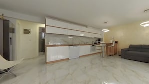 A modern kitchen with white cabinets, a marble countertop, and a built-in oven. There is a grey sofa and a small table with chairs in the living area. - Charming 3-bedroom House Rental in Málaga, Spain (Málaga)