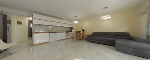 A modern kitchen with white cabinets, a marble countertop, and a built-in oven. There is a grey sofa and a small table with chairs in the living area. - Charming 3-bedroom House Rental in Málaga, Spain (Málaga)