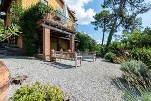 A building with a balcony, outdoor seating, and a gravel ground. - Villa la Leccia by MMega (Massarosa)