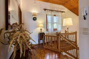Un escalier en bois avec une rampe, un pot de fleurs, deux lampes, un radiateur et un téléphone fixé au mur.