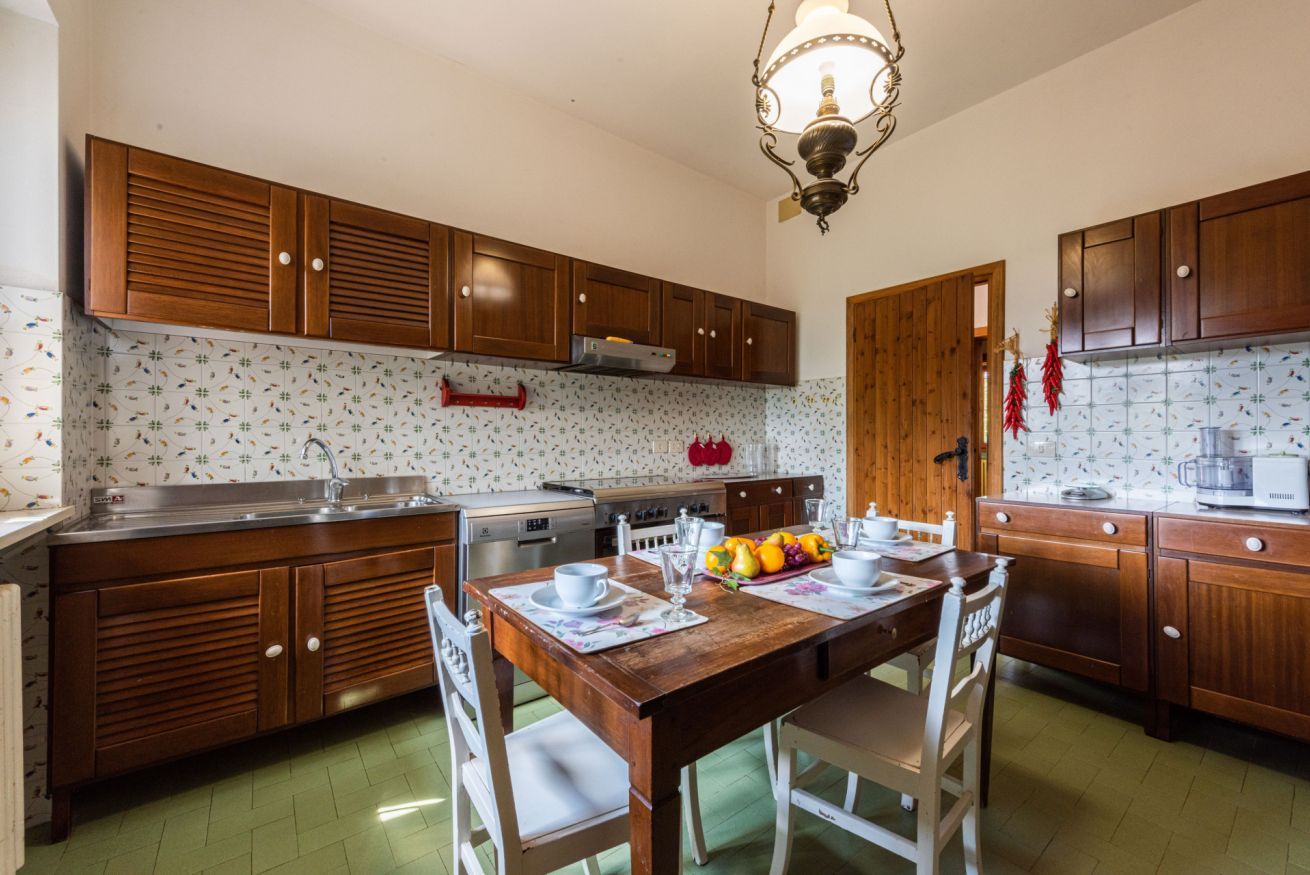 A kitchen with wooden cabinets, a dining table set for four, and a hanging light fixture.
