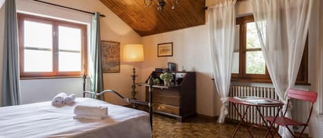 Ein Zimmer mit einem Bett, einem Schreibtisch, einem Stuhl, einem Heizkörper und einem Vorhangfenster.