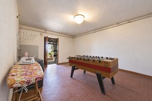 A room with a foosball table, a table with a floral tablecloth, and a laundry area with a drying rack. - Villa la Leccia by MMega (Massarosa)