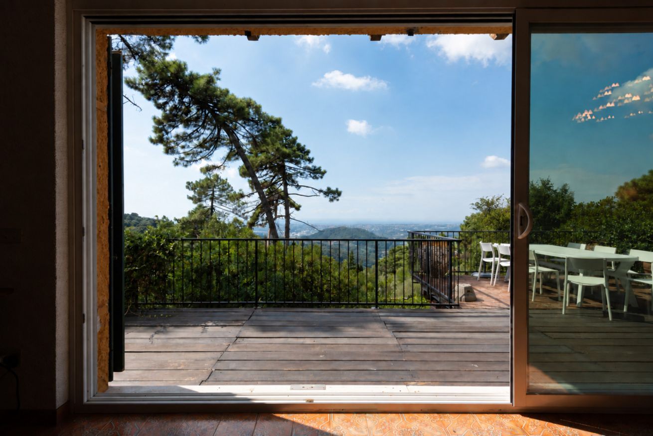A view through a glass door to an outdoor deck with a wooden floor, a metal railing, and a table and chairs set up for dining.