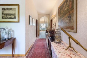 Un couloir orné de tableaux encadrés, un tapis rouge, une table en bois sur laquelle est posée une lanterne, et un télescope en laiton.