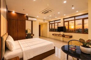 A hotel room with a bed, a TV, a desk, and a window with a city view. - O Lily Hotel (Ninh Binh)