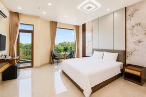 Ein Hotelzimmer mit Bett, Schreibtisch mit Fernseher, Balkon mit Stühlen und Blick ins Grüne.