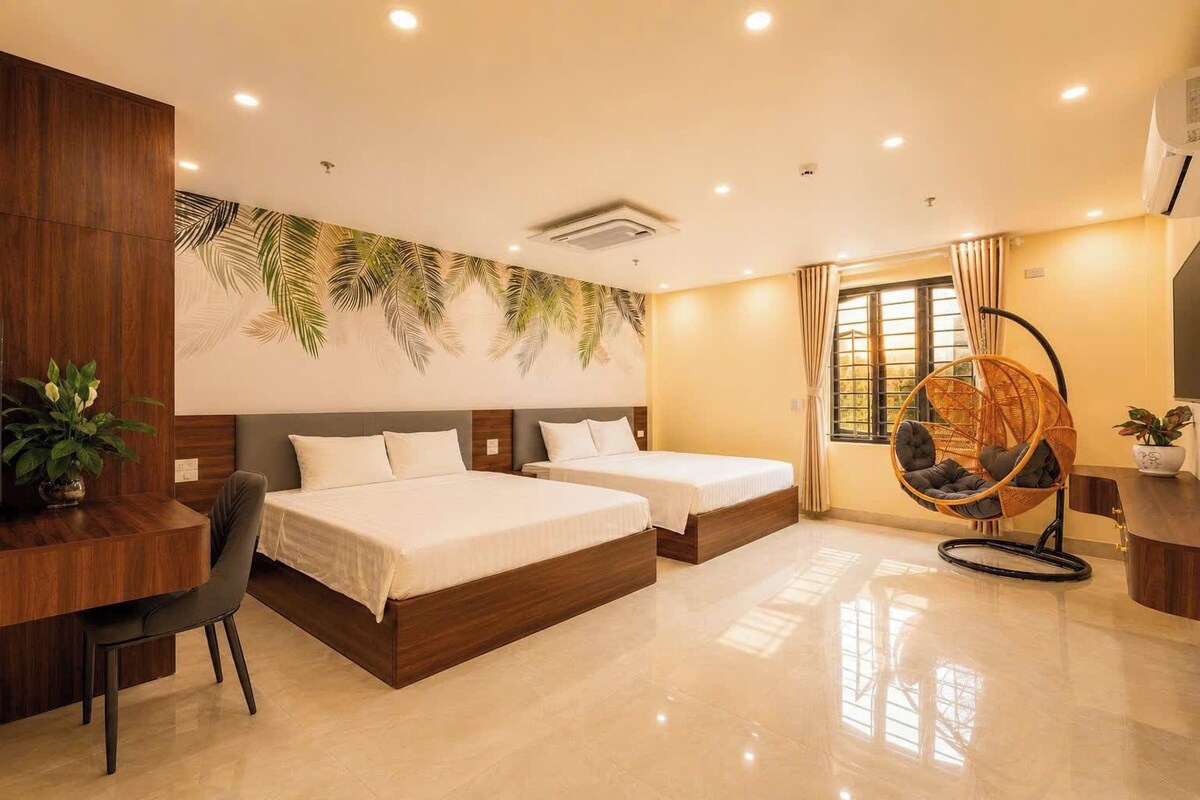 A hotel room with two beds, a desk, a chair, a hanging chair, and a large window.