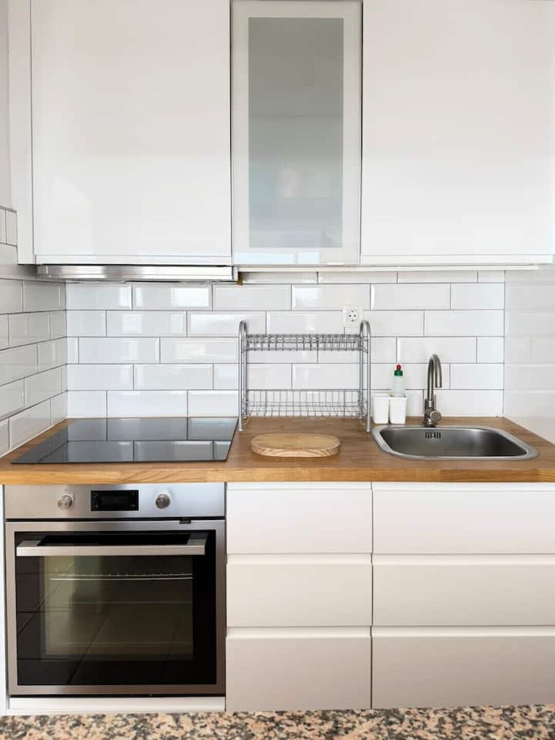 Een keuken met witte kasten, een roestvrijstalen oven, een spoelbak en een houten aanrecht.
