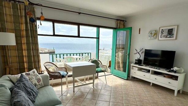 Ein Wohnzimmer mit einer Couch, einem Fernseher, einem Esstisch, Stühlen und einem Balkon mit Blick.