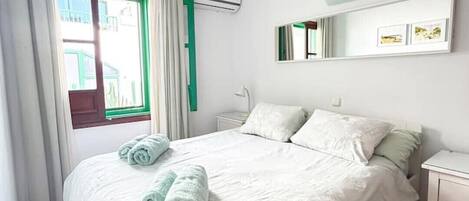A bedroom with a bed, a nightstand, a mirror, and an air conditioning unit.
