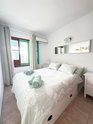 A bedroom with a bed, a nightstand, a mirror, and an air conditioning unit. - Roca Negra (Tías)