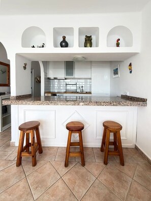 A kitchen with a white island, two wooden stools, and decorative items on the wall. - Roca Negra (Tías)