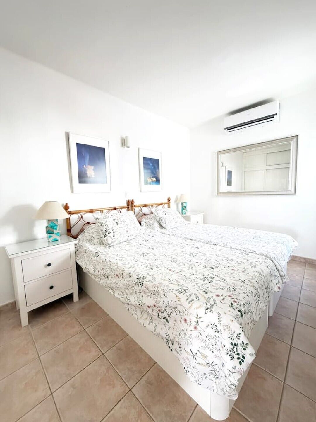 Ein Schlafzimmer mit einem Bett, Nachttischen, einem Spiegel und zwei gerahmten Bildern an der Wand.