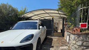 A white Porsche parked in a stone-paved driveway with a covered entrance and a stone wall. - Itaca House - ChiacchioProperty (Villammare)