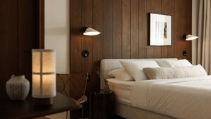 Una habitación de hotel con una cama, una silla, una mesa y lámparas fijadas a la pared.