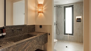Un baño moderno con lavamanos de mármol, un espejo grande, una lámpara de pared y zona de ducha.